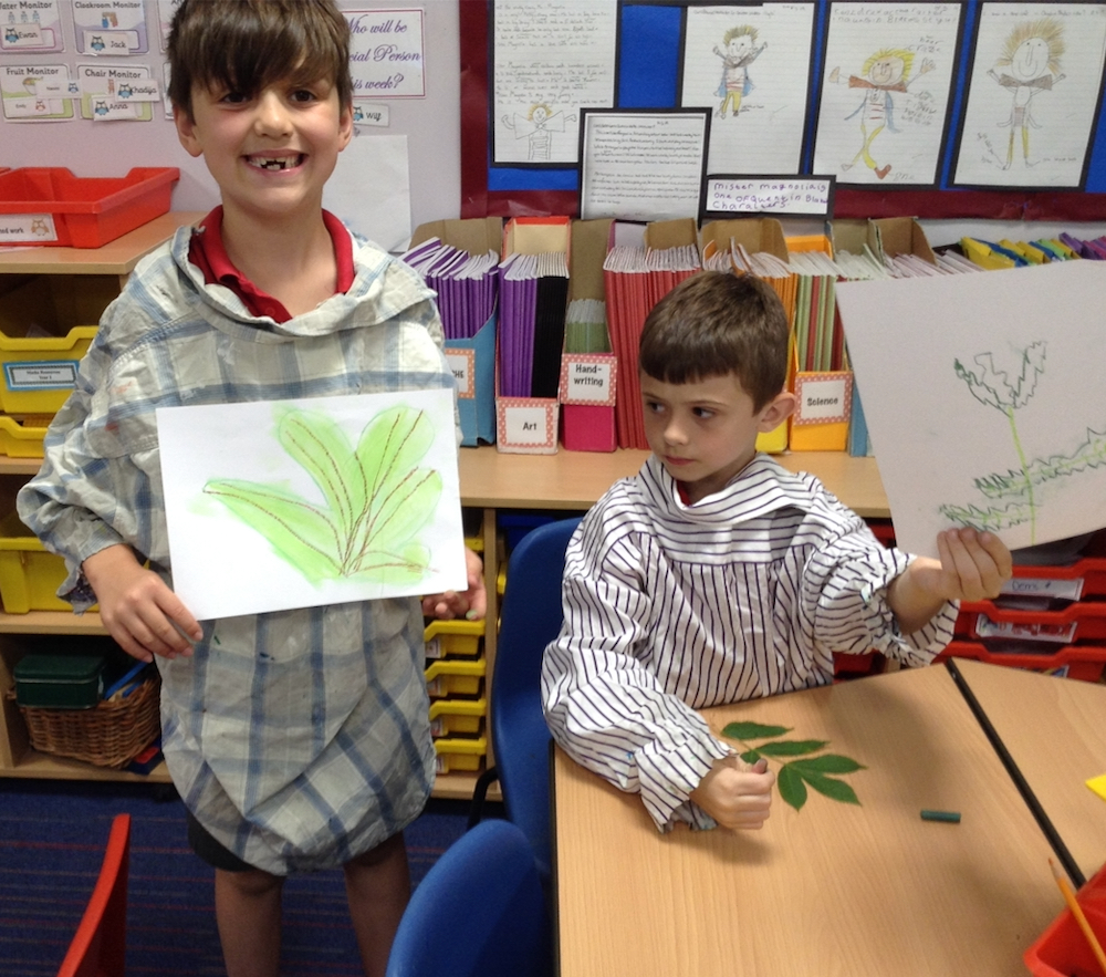 Year Two boy holding up his pastel drawing of a leaf in a year one and two classroom at Hauxton Primary school with teacher Pamela Stewart for Inspire
