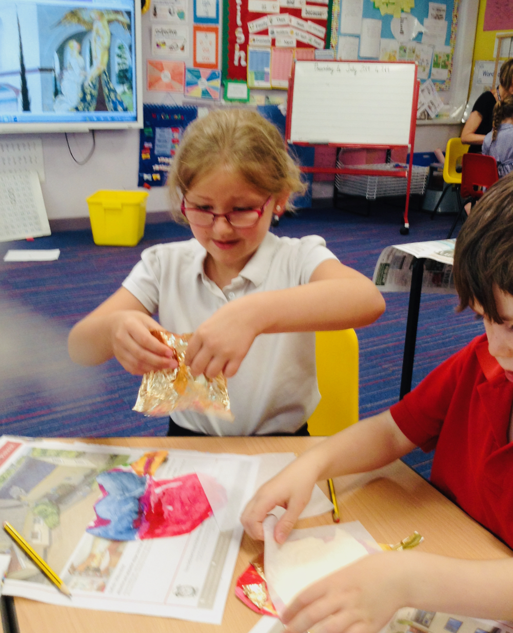 A Year One girl gently rips gold leaf to apply to her brightly painted leaf at Hauxton Primary School for Inspire with Pamela Stewart
