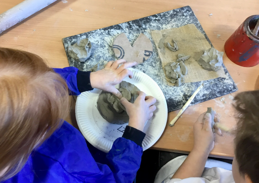 Image of a year one pupil's hands working with grey school clay pushing their thumbs into the damp clay