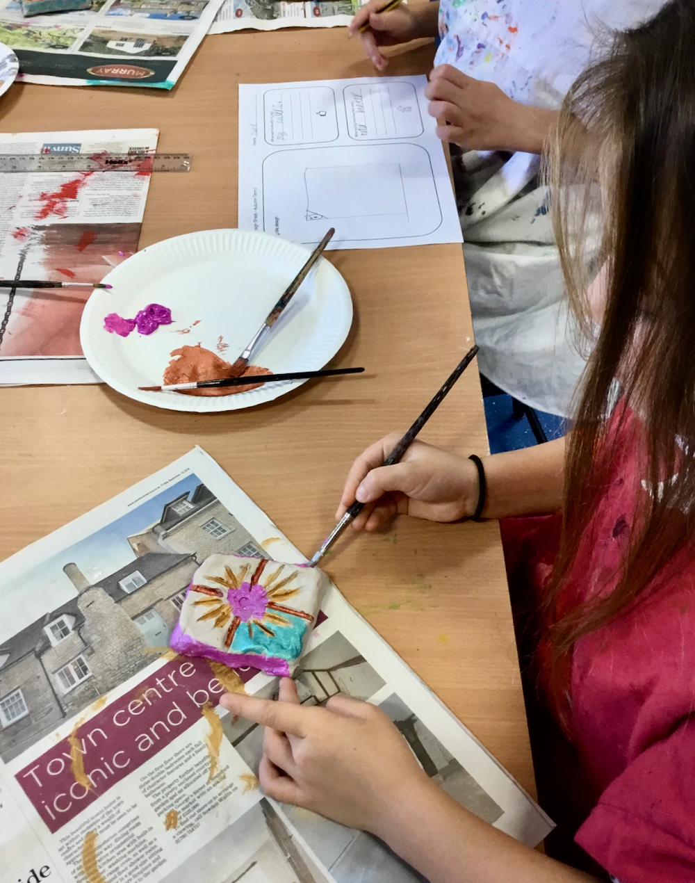 A Year Two Pupil painting with school paint on unfired clay in a classroom taught by Sue Brown